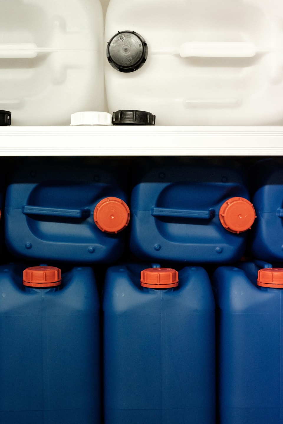 White and blue plastic jerry cans stacked on a shelf.