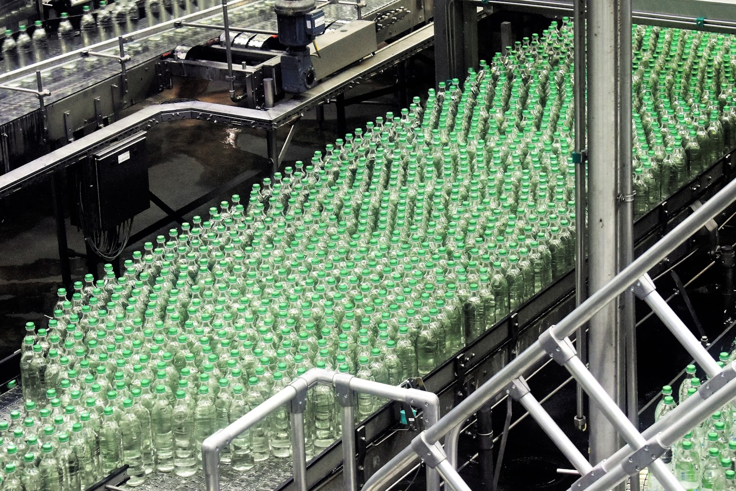 Plastic bottles with green caps on a conveyor belt in a factory.