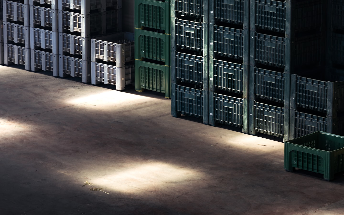 Stacks of grey and green plastic storage crates in a warehouse.